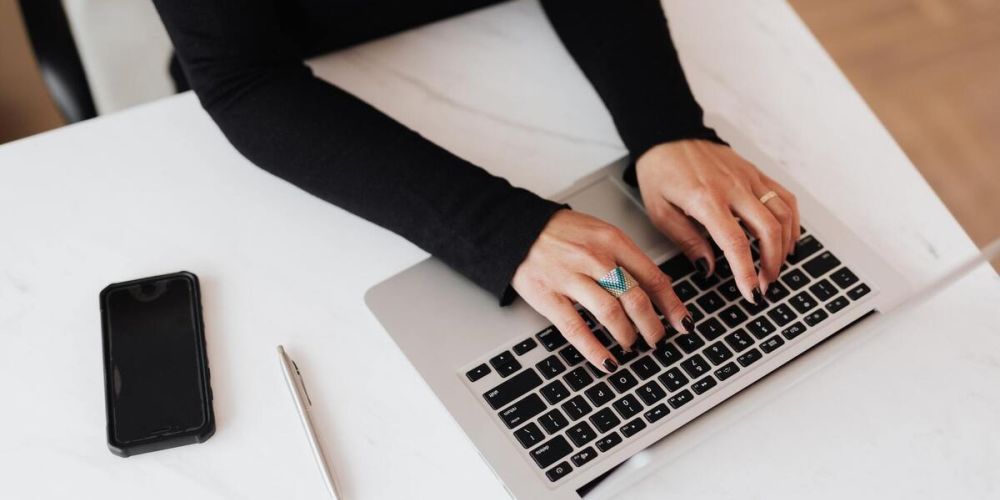 Dłonie kobiety piszącej na klawiaturze laptopa.